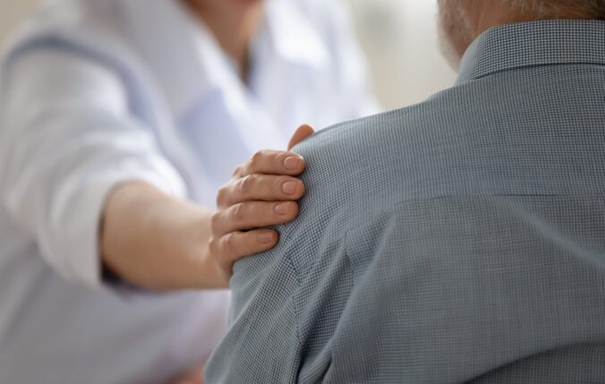 Nyrs neu ddoctor yn rhoi llaw ar ysgwydd y claf mewn cefnogaeth
